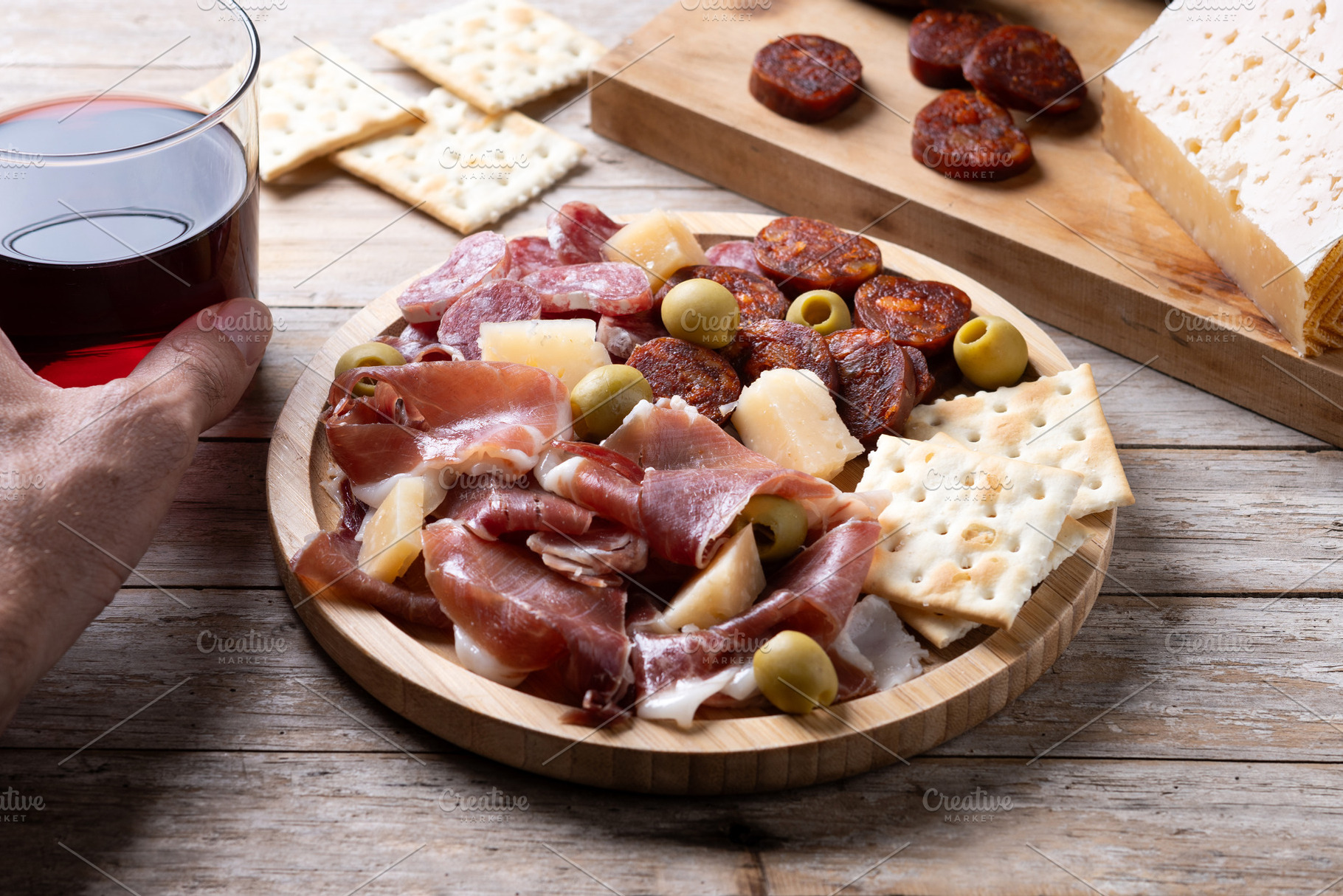 Hand picking up glass of red wine beside Spanish charcuterie board, a Food & Drink Photo by etorres69