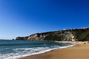 Golden sandy beach with waves and cliffs in picturesque Nazare, Portugal settin, a Photo by AS photostudio