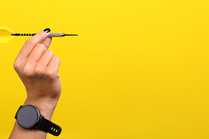 Close-up of a hand holding a dart against a bright yellow backgr, a Sports & Recreation Photo by Ales Munt