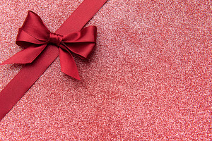 Red satin ribbon bow on sparkling glitter background, a Photo by Olena Rudo