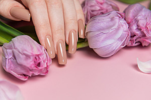 Woman showing nude manicure and pink tulips on pink background, a Beauty & Fashion Photo by Olena Rudo
