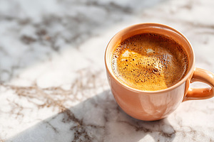 Morning coffee in a ceramic cup on a marble table catching the sunlight, a Food & Drink Photo by AlyaAnd