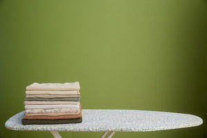 Folded clothes on ironing board with olive green backdrop, a Photo by Alliance Images