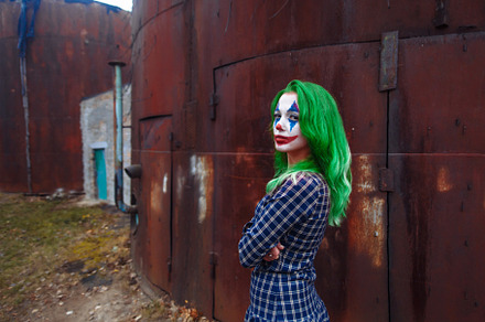 Portrait of a greenhaired girl in chekered dress with joker makeup on a rusty m