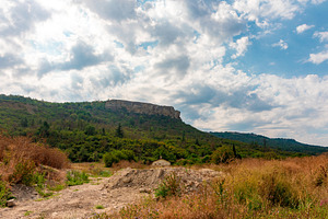 Wide view of a green hill with rocky cliffs beneath a dramatic cloudy sky, natu, a Nature Photo by Ales Munt