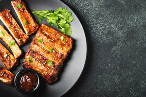 Hot grilled spare ribs from a summer BBQ served on a plate with sauce. Top view, a Food & Drink Photo by Budarinphoto