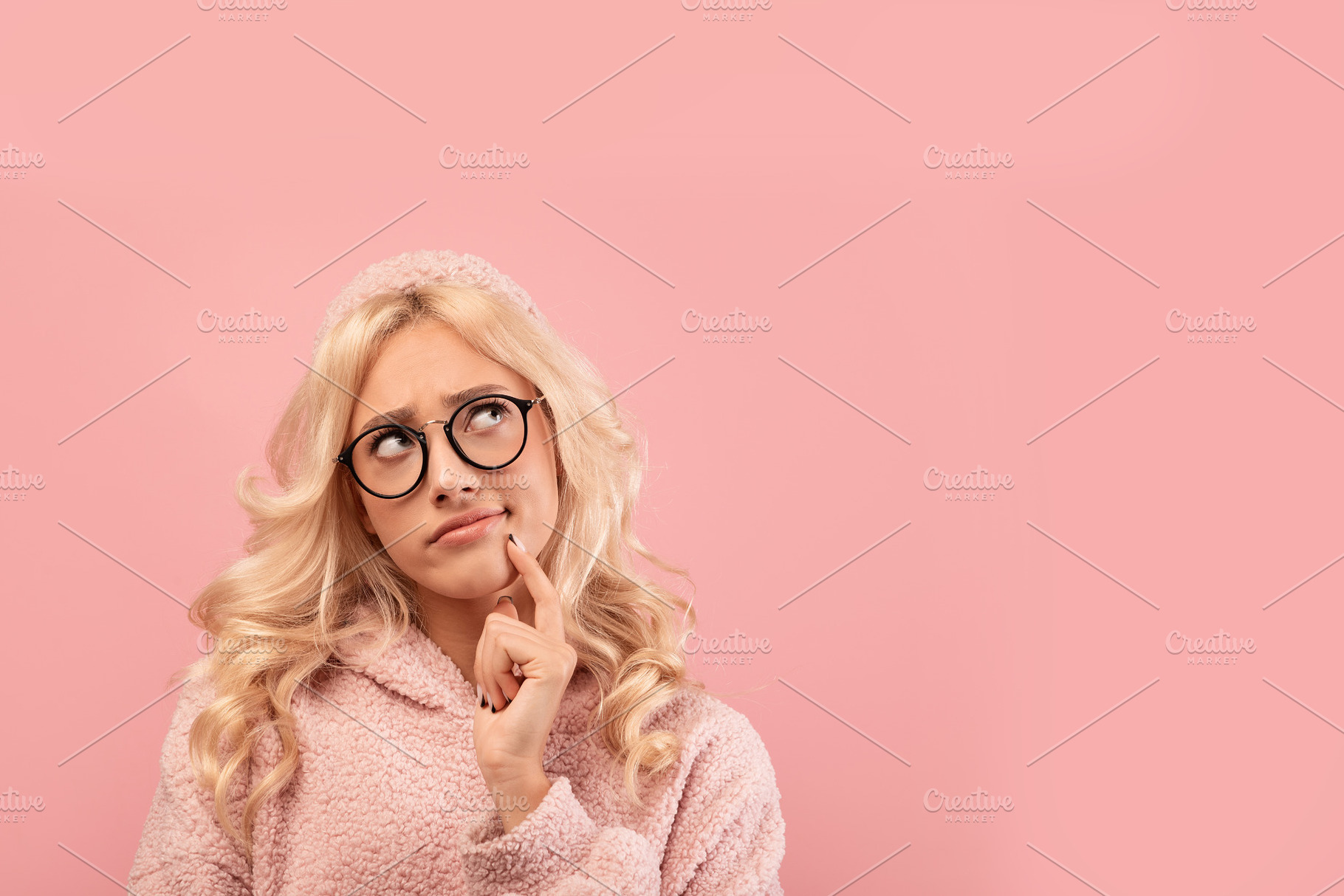 Thoughtful blonde woman in glasses looking at copy space, standing over pink st, a Photo by Prostock-Studio