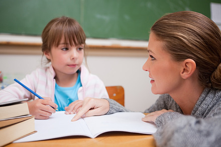 Schoolgirl writing a while her teacher is talking, a Photo by wavebreak