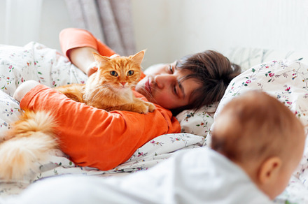 Man with baby and ginger cat in bed.