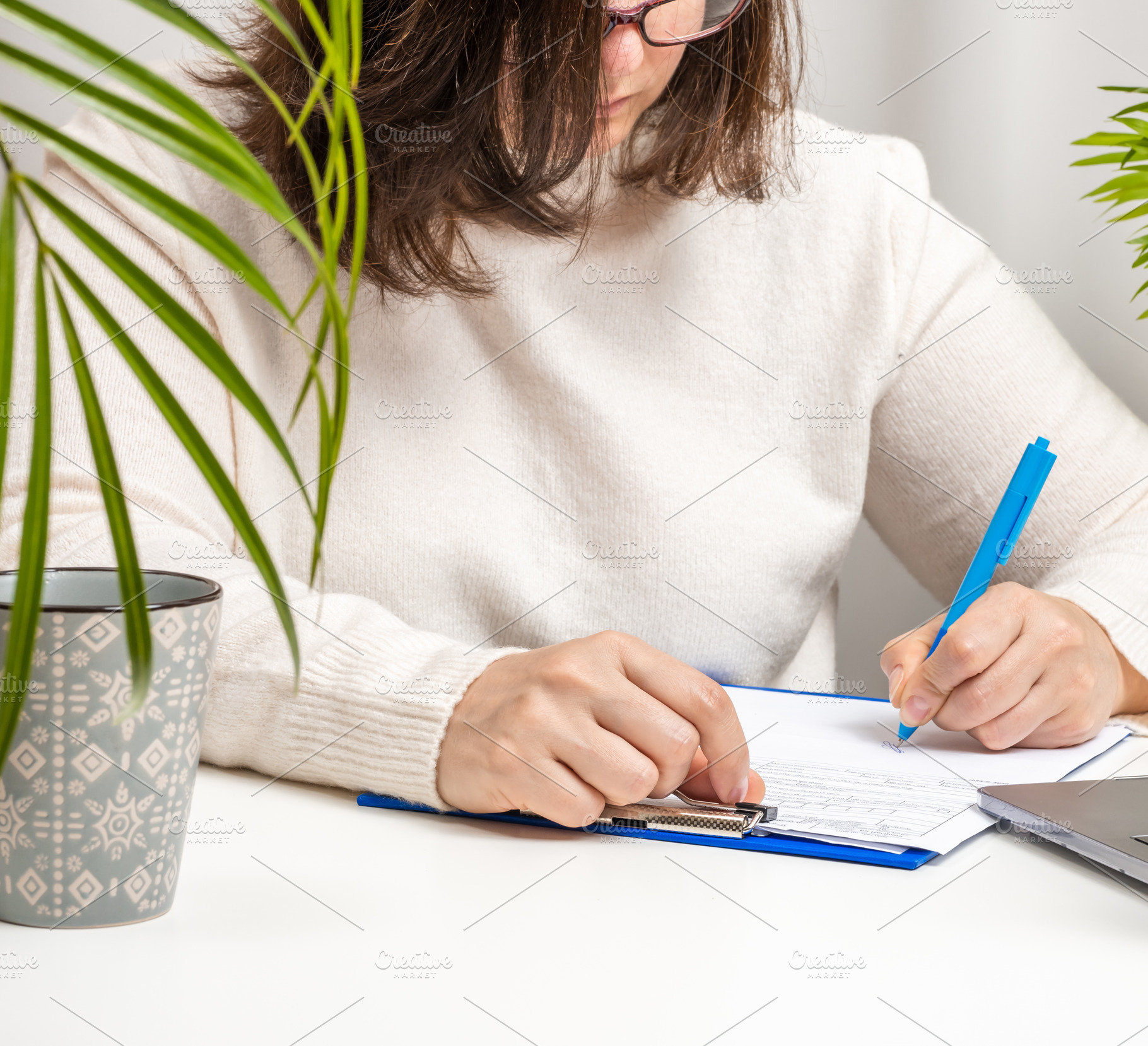 woman in a white sweater and glasses signs documents on the tabl, a Business Photo by ndanko