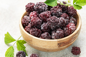 Frozen blackberries in wooden bowl with green leaves, a Food & Drink Photo by Olena Rudo