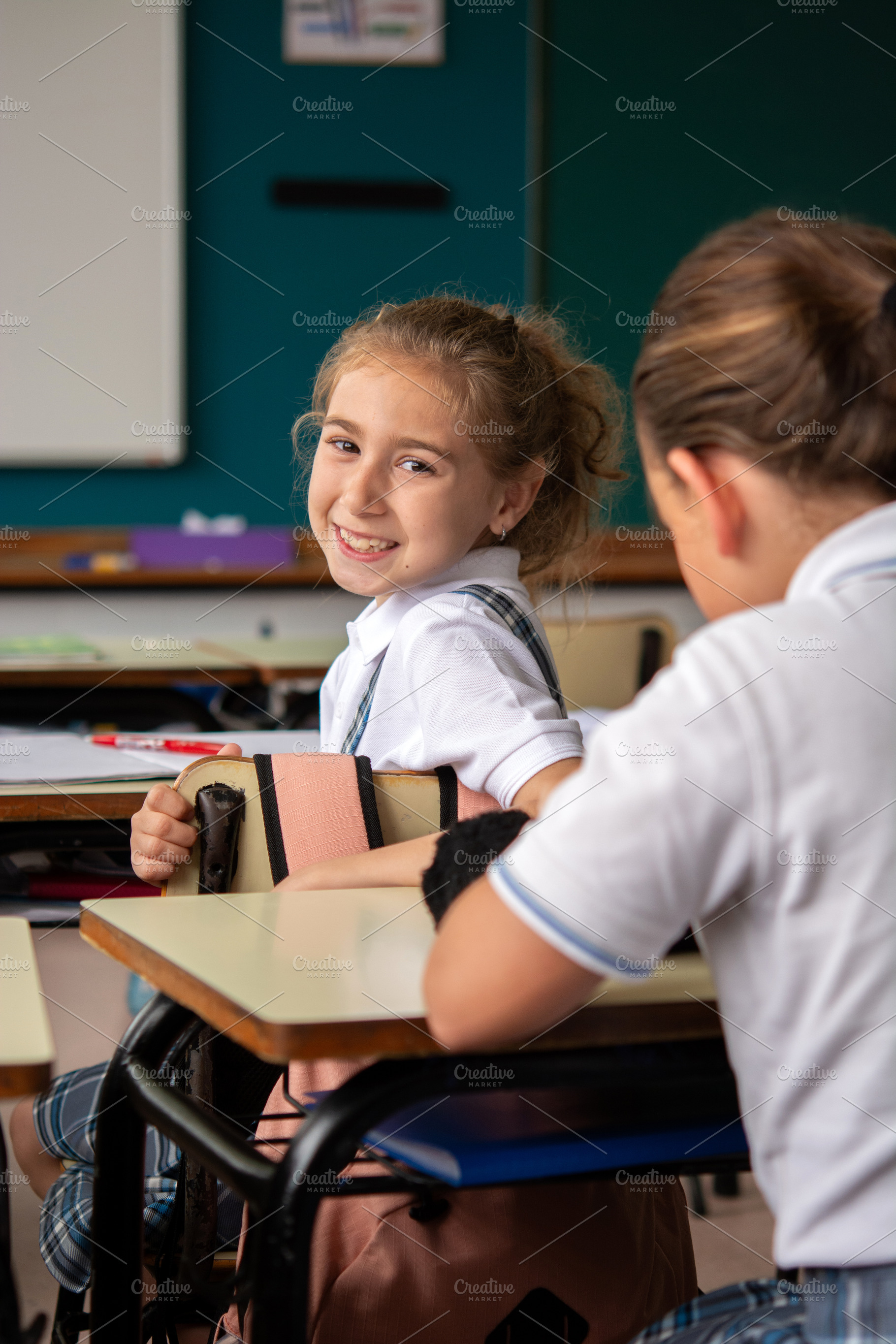 Smiling Elementary School Girl Looking Back at Classmate During Lesson, a School & Education Photo by etorres69