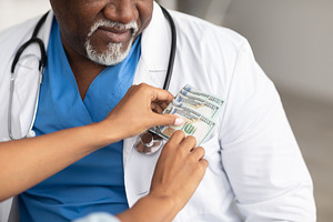 Black female hand putting money in doctor's pocket, closeup, a Photo by Prostock-Studio