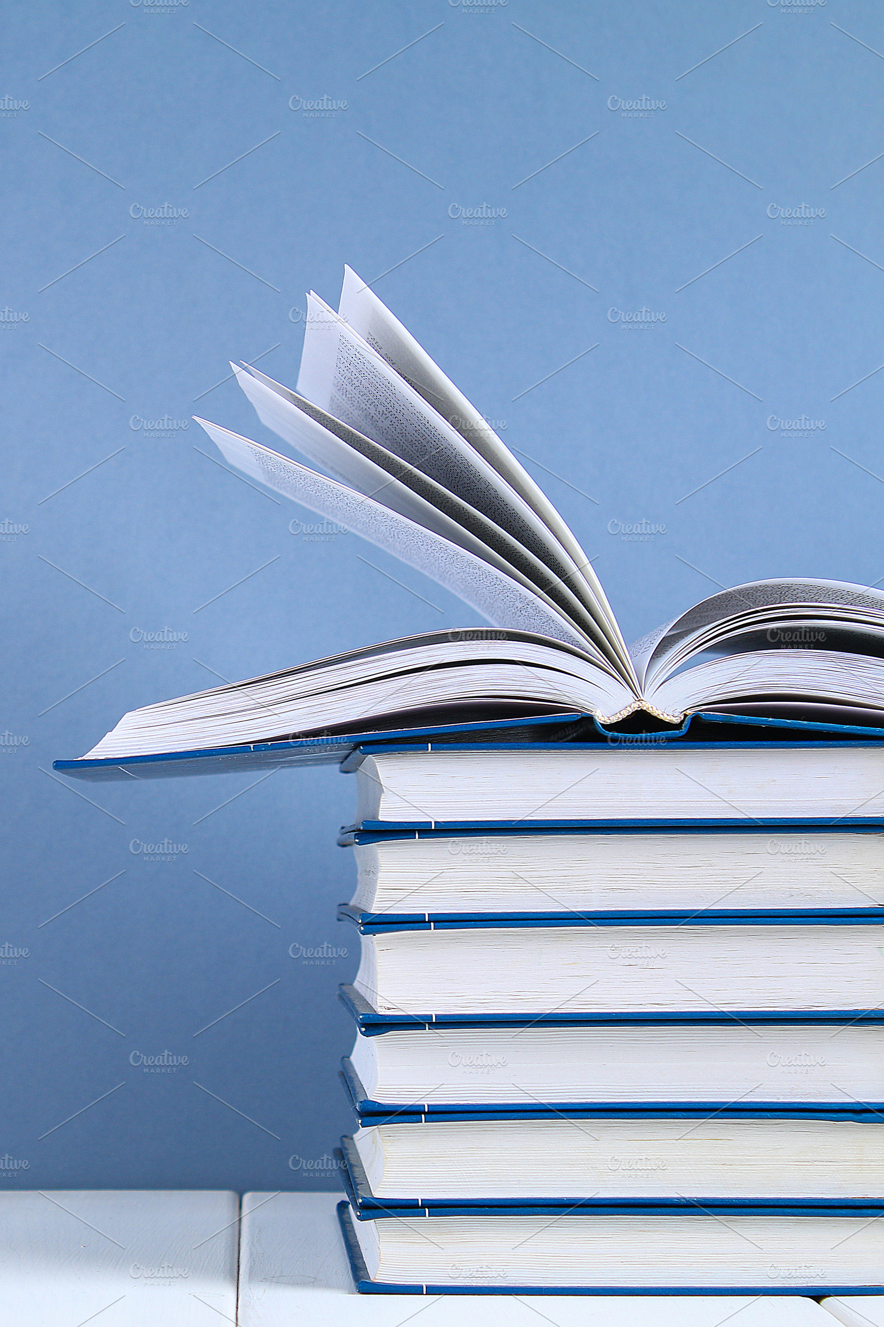 A stack of books on blue background., a School & Education Photo by Detriana