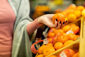 Cropped of woman shopping at supermarket, choosing tangerine, a Photo by Prostock-Studio