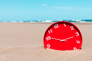a red clock sinks into the sand on an empty beach, a Photo by Nito