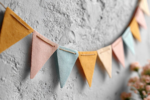 Colorful paper bunting flags hanging against a textured wall at a festive gathe, a Background Photo by AlyaAnd