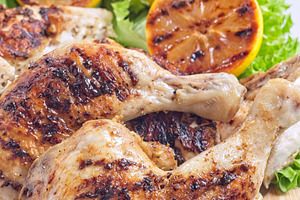 Grilled chicken legs and breast with lemon and lettuce on wooden board, vertica, a Food & Drink Photo by iuliia_n