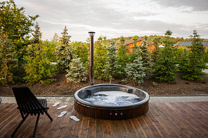 Outdoor hot tub on wooden deck surrounded by lush greenery under a cloudy sky, a Photo by AS photostudio