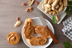 Freshly sliced bread spread with peanut butter on wooden t, a Food & Drink Photo by Davizro's Market