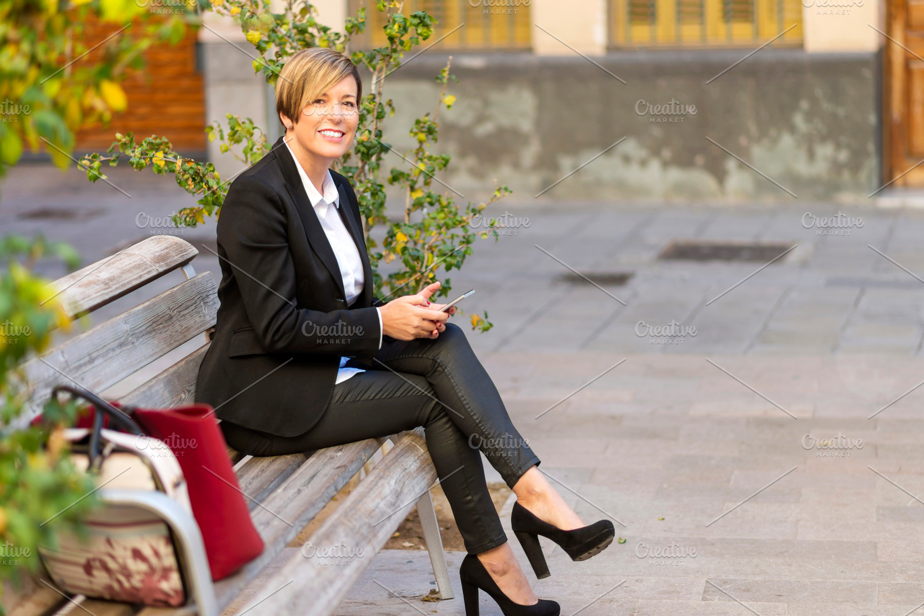 Businesswoman sitting on bench using smartphone, a Photo by RF Images