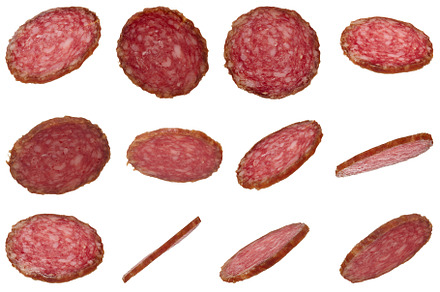 Many thin slices of smoked salami sausage scattered on isolated