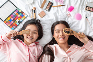 Glad satisfied young asian female and teenage girl, close eye with comb, lie on, a Photo by Prostock-Studio