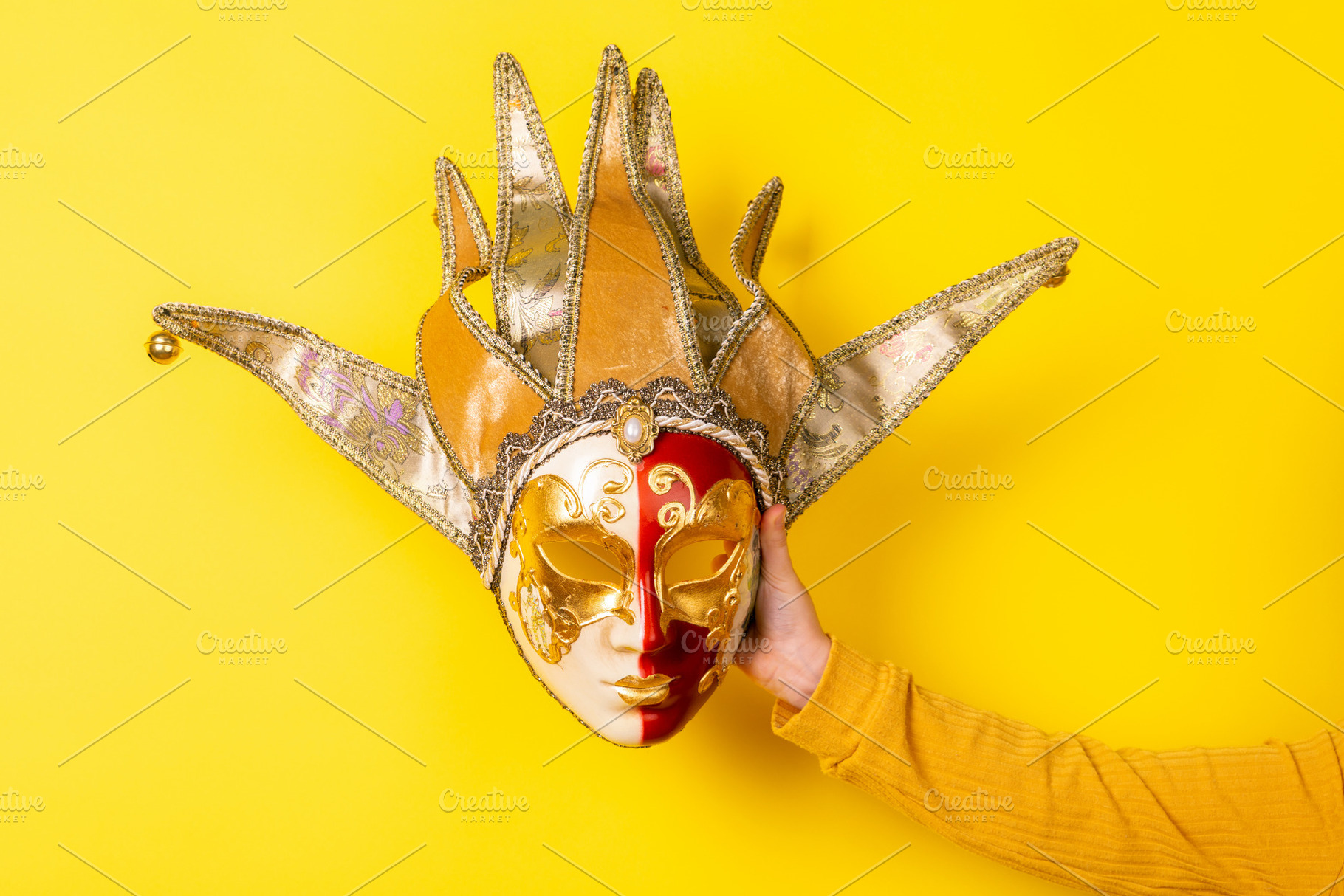 Hand holding ornate Venetian jester mask against vibrant yellow, a Holiday Photo by Ales Munt