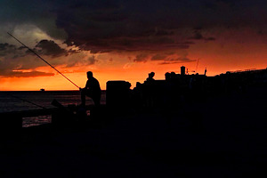 Silhouettes of fishermen casting lines under dramatic sunset sky, a Nature Photo by DanFLCreativo