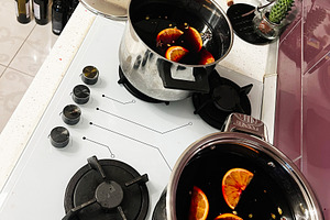Two pots simmering mulled wine with orange slices in a cozy modern kitchen, a Photo by AS photostudio
