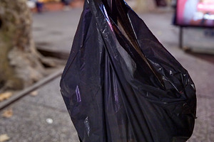 Black trash bag hanging on tree in city at night, a Background Photo by DanFLCreativo