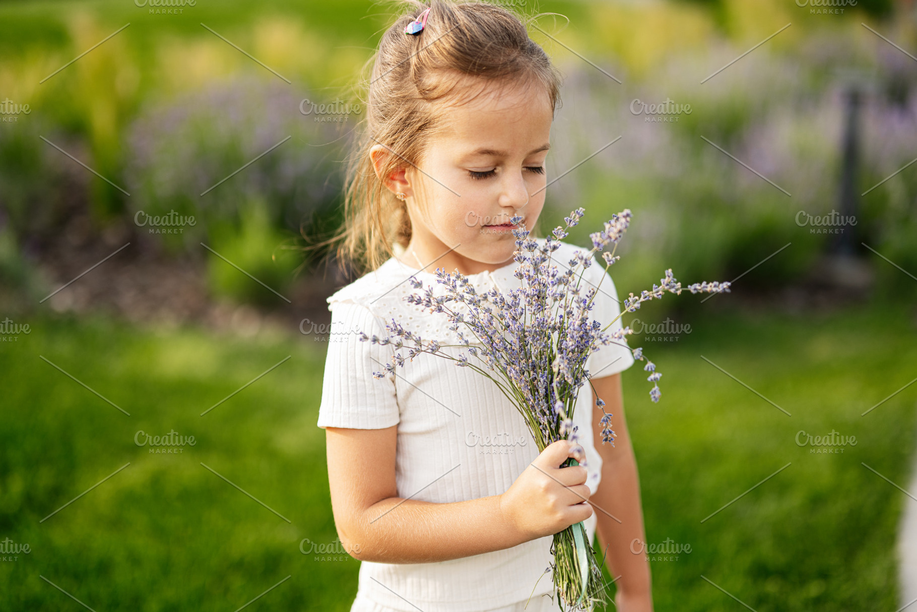 Little girl enjoying the scent of lavender in a sunny garden, a Photo by AS photostudio