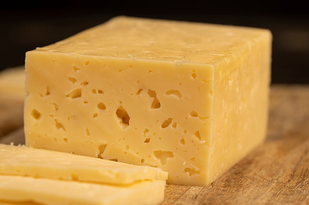 cheese with holes for cooking, pieces of sliced cheese on a cutting board, side