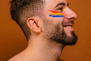 Smiling man celebrating pride with rainbow face paint, a Photo by karrastock