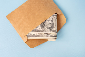 Stash of money in dollar bills coming out of an envelope on a blue background., a Business Photo by Artsaba Family