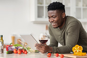 Happy Black Man Using Digital Tablet And Drinking Red Wine In Kitchen, a Photo by Prostock-Studio (Thumbnail 1 of 2)