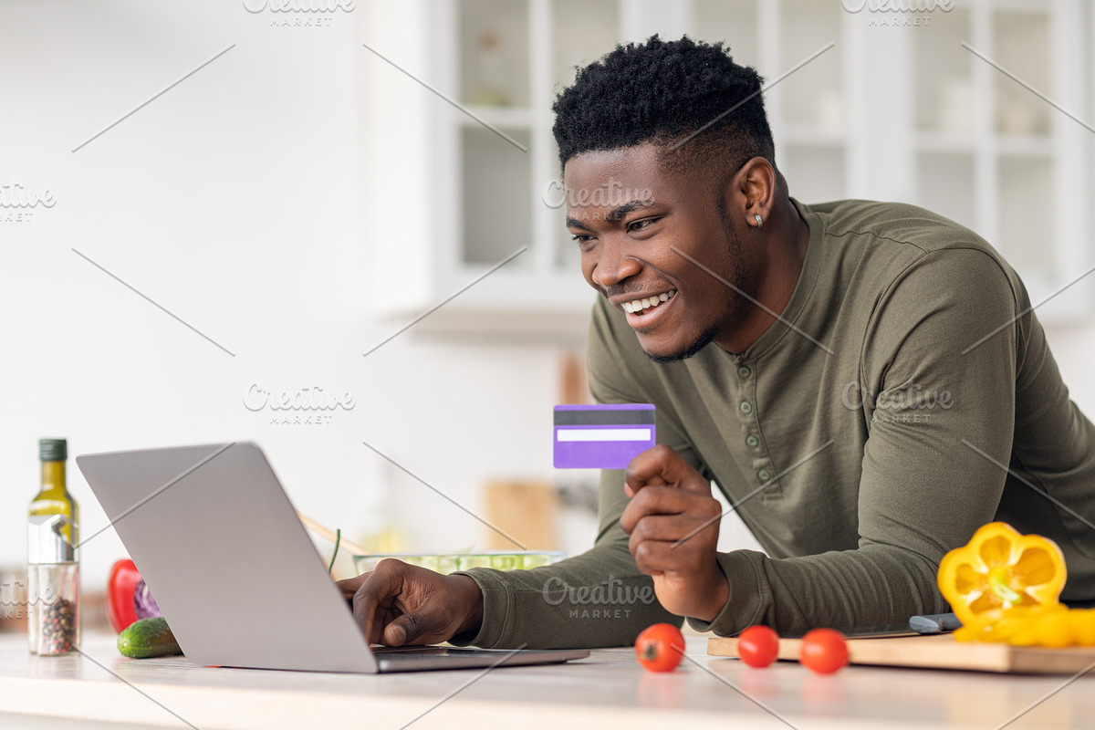 Ordering Food Online. Black Guy Using Laptop And Credit Card In Kitchen, a Photo by Prostock-Studio (Photo 1 of 2)