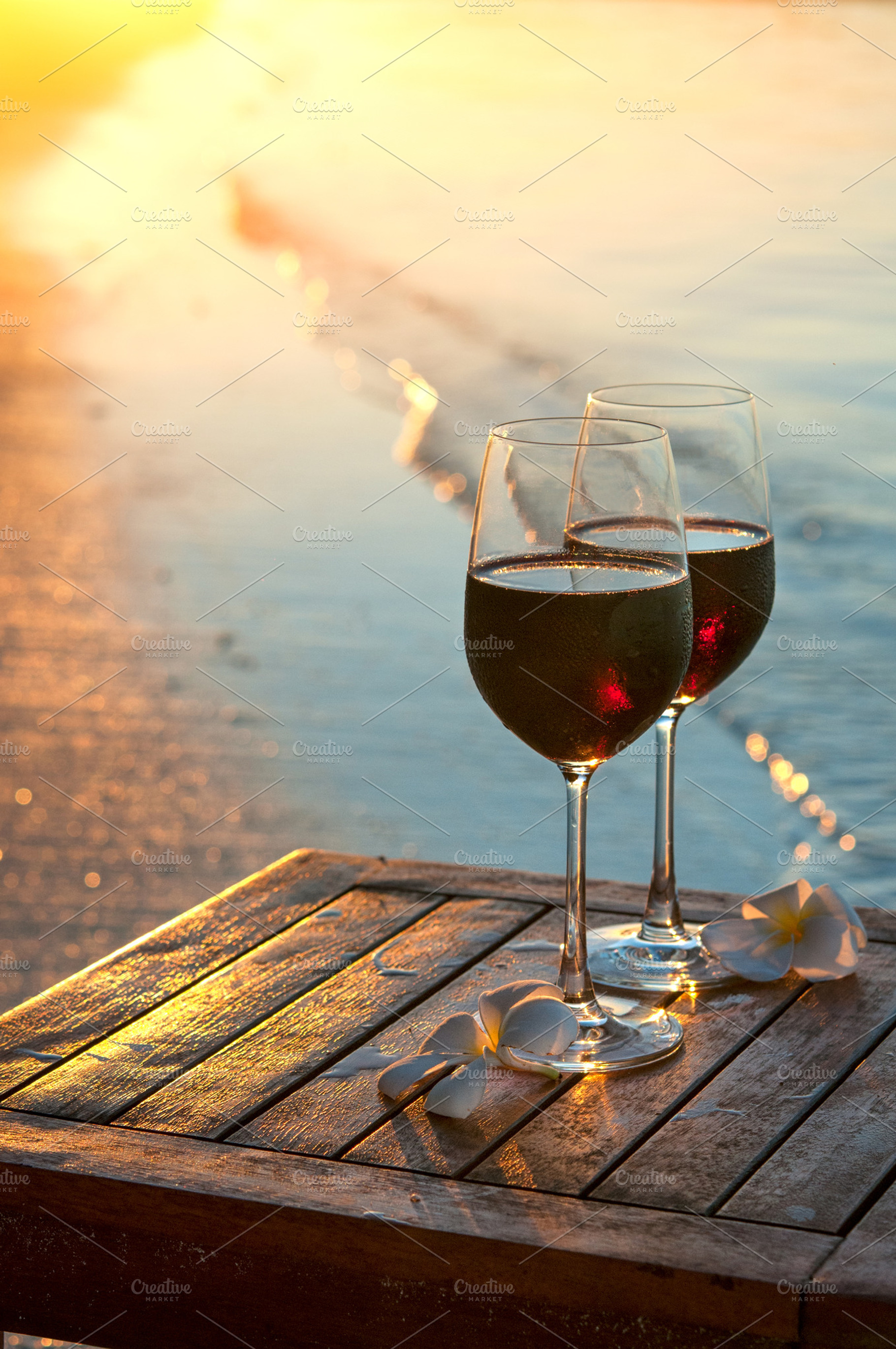 Romantic beach scene: two glasses of red wine at sunset near water, a Photo by Edgieus