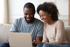 Couple enjoying a joyful moment while using a laptop in a cozy living room, a Photo by AlyaAnd