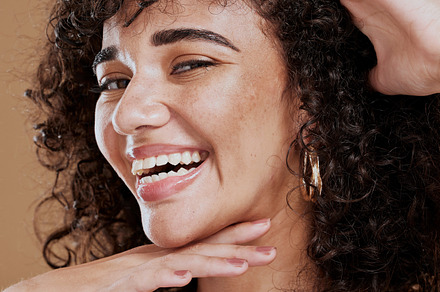 Portrait, woman and face makeup, happy and skincare with beauty, smile and happy in brown studio background. Hair care, afro or curls with healthy skin, glow and happiness model with facial cosmetic, a Photo by Peopleimages.com