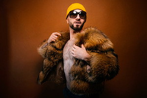 Man posing with furry jacket yellow beanie sunglasses, a Photo by karrastock