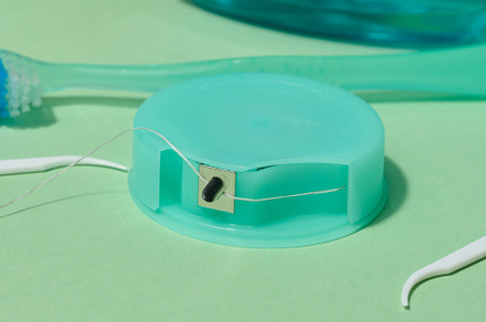 A turquoise dental floss container with floss extended, along wi