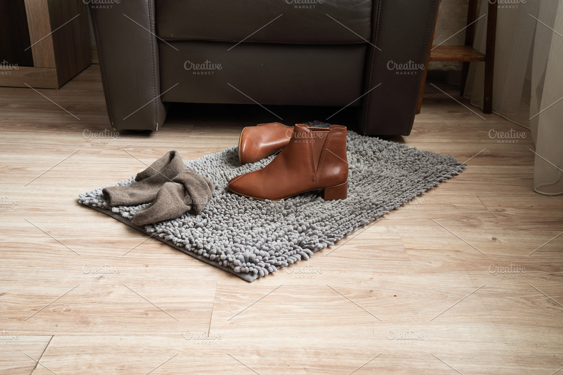 Pair of brown leather ankle boots on rug in cozy living room, an Industrial Photo by MDBildes