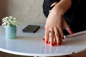 Womans hands with red nails resting on table beside flowers and smartphone, a Person Photo by Photostock