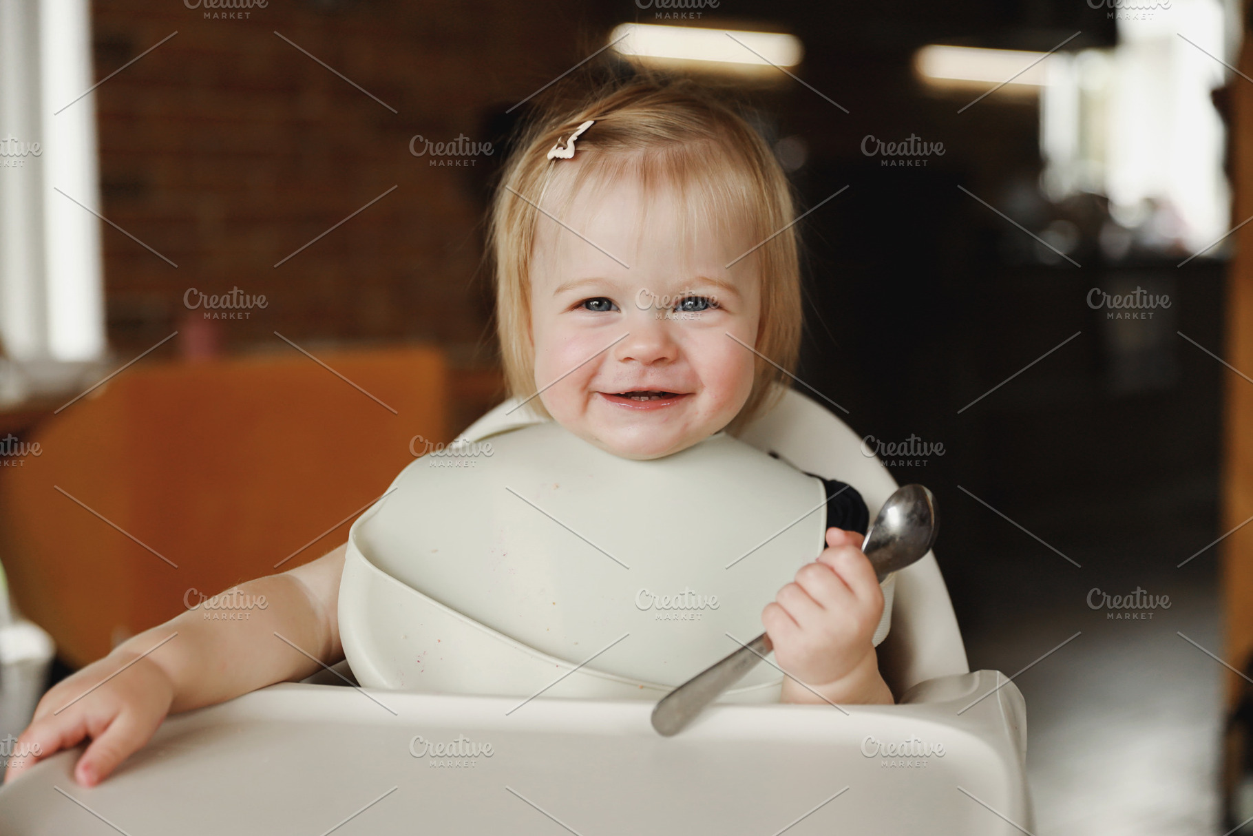 Infant girl or toddler sitting on high chair. Eating food by herself using spoo, a Person Photo by Lenor4ik