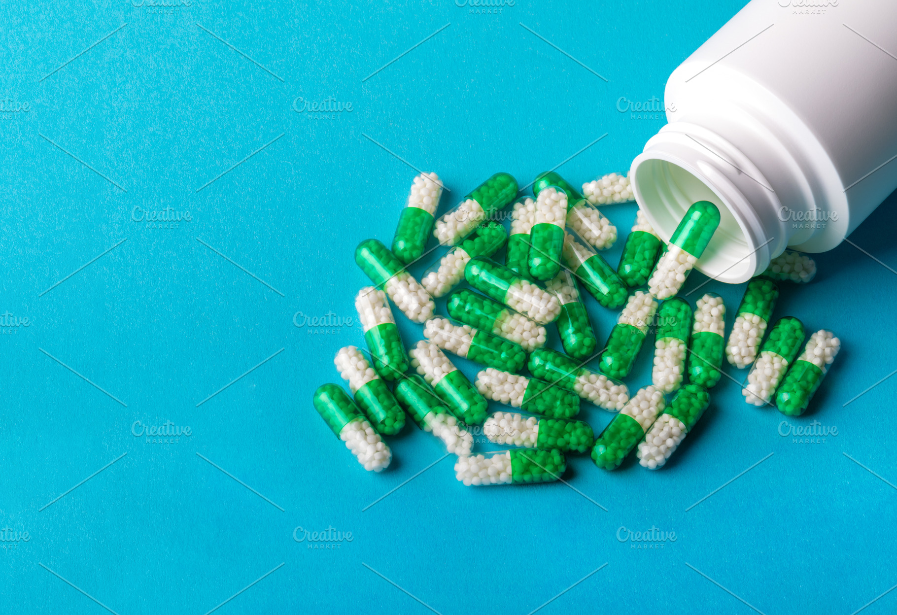 White plastic bottle with green and white capsules spilled on blue background,, a Health & Medical Photo by Ales Munt