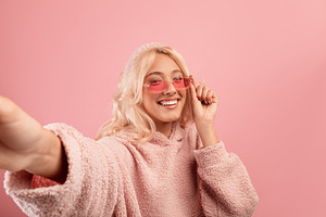 Cheerful stylish woman making selfie, wearing colorful glasses and hoodie, smil, a Photo by Prostock-Studio