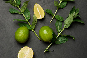 Whole and cut limes with fresh mint leaves arranged on a dark te, a Food & Drink Photo by ndanko