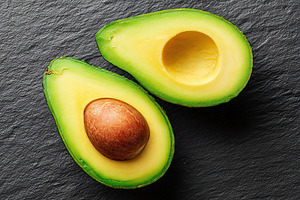 Halved avocado on dark slate background showcasing its creamy texture and healt, a Food & Drink Photo by AlyaAnd