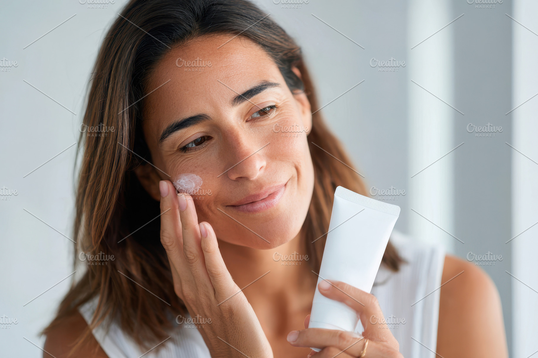 Woman applying skincare cream with a smile, a Person Photo by AlyaAnd